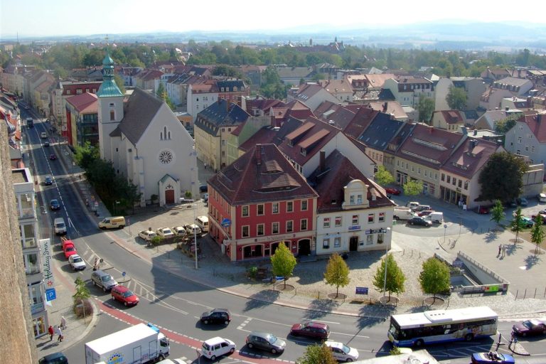 Blick auf einen Platz mit bunten Gebäuden, Bäumen und Straßenverkehr in Bautzen.