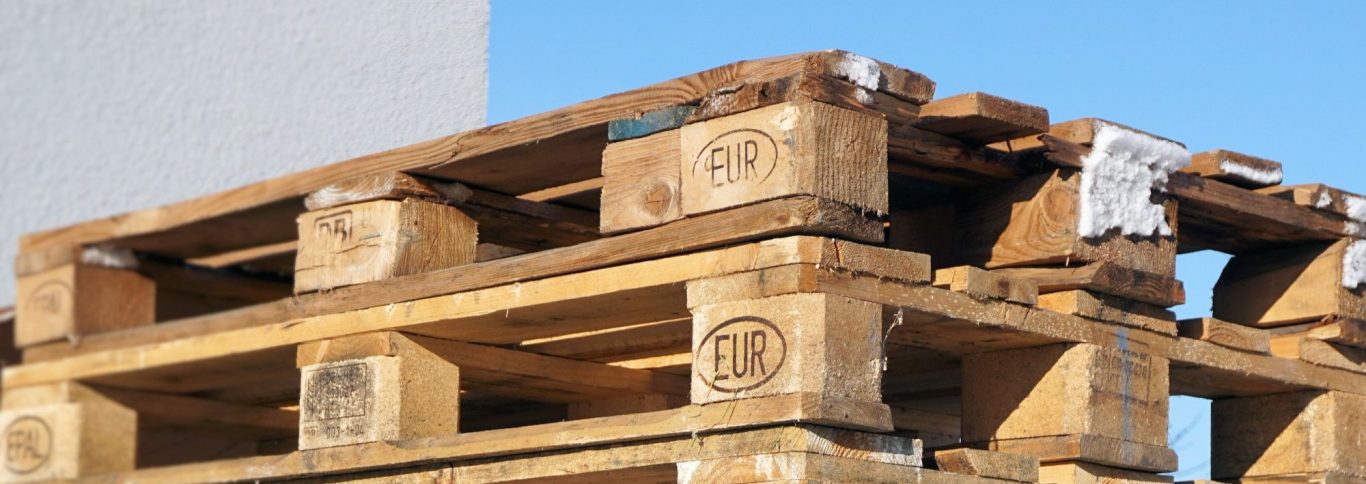 Holzpalette mit mehreren Lagen, teilweise beschädigt und im Freien gelagert.