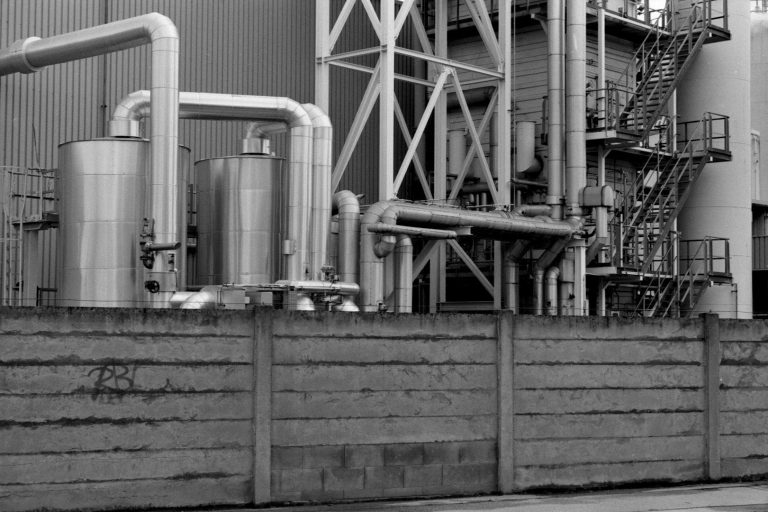 Industriegelände mit Rohren und großen Silos in Schwarz-Weiß.