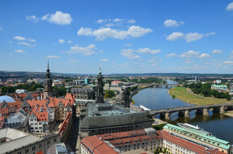 Blick auf die Altstadt von Dresden mit Brücke und Fluss, unter blauem Himmel mit Wolken.