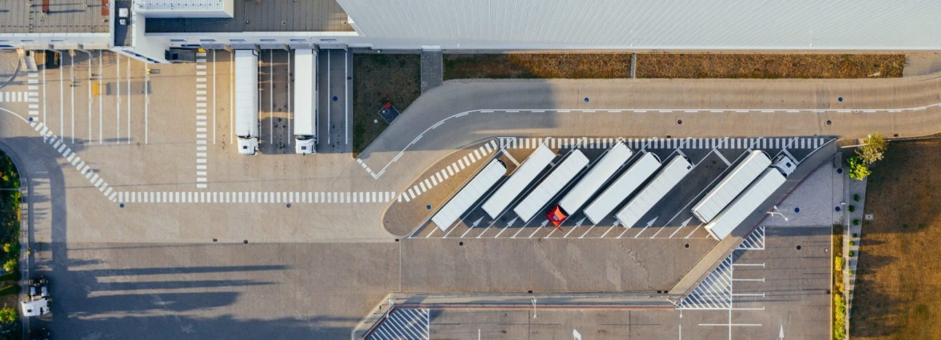 Speditionsdelikte Erfurt | Transportdiebstahl Luftaufnahme eines Parkplatzes mit mehreren Lkw und einem roten Fahrzeug.