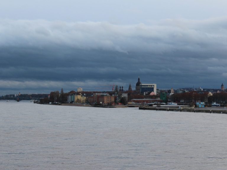 Silhouette einer Stadt am Wasser unter bewölktem Himmel.