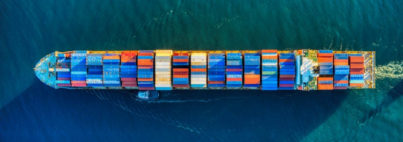 Was ist Logistik? ➡︎ Klick Ein großer Frachter mit bunten Containern fährt auf blauem Wasser.