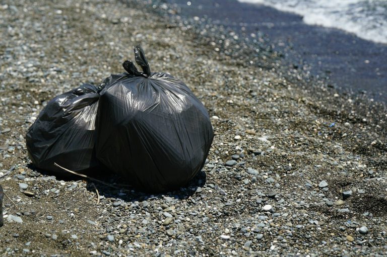 Zwei schwarze Müllsäcke liegen am Strand auf Kieselsteinen.