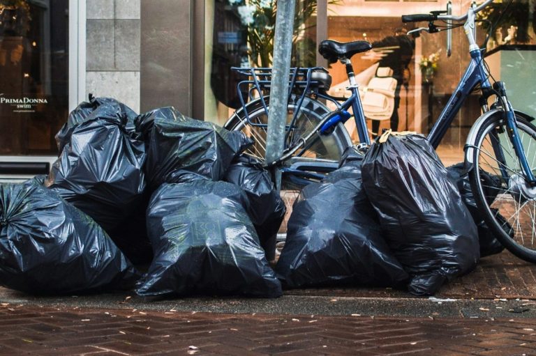 Schwarze Müllsäcke auf dem Bürgersteig neben einem Fahrrad.