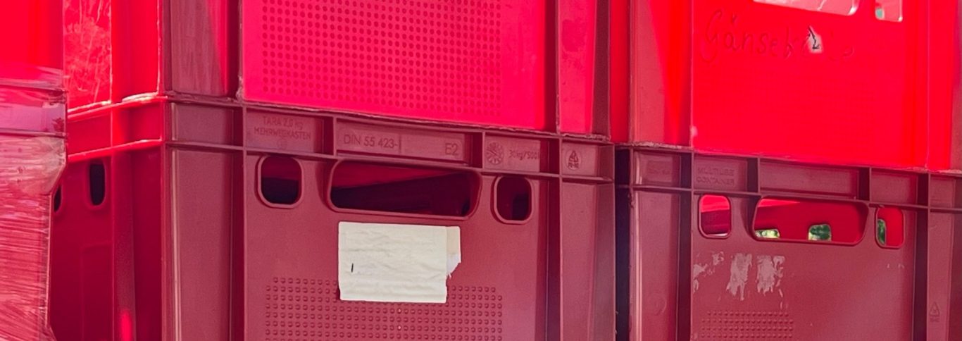 Was ist Logistik? ➡︎ Klick Rote Lagerkisten übereinander gestapelt, mit einem weißen Etikett auf einer Kiste.