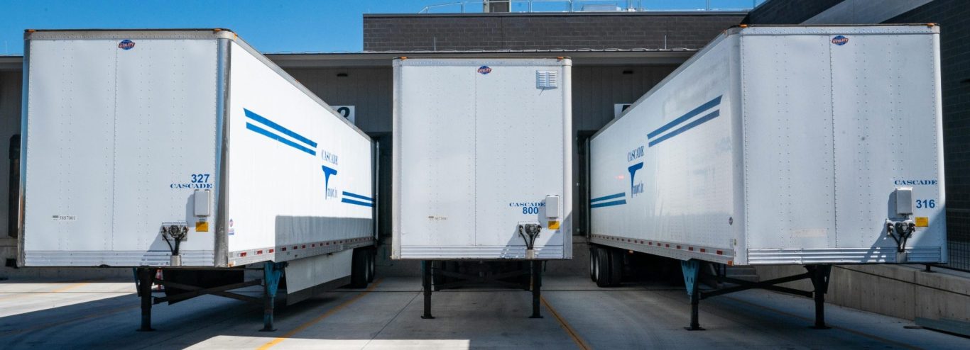 Speditionsdelikte Dresden| Transportdiebstahl Drei weiße Lkw-Anhänger nebeneinander vor einem Gebäude.