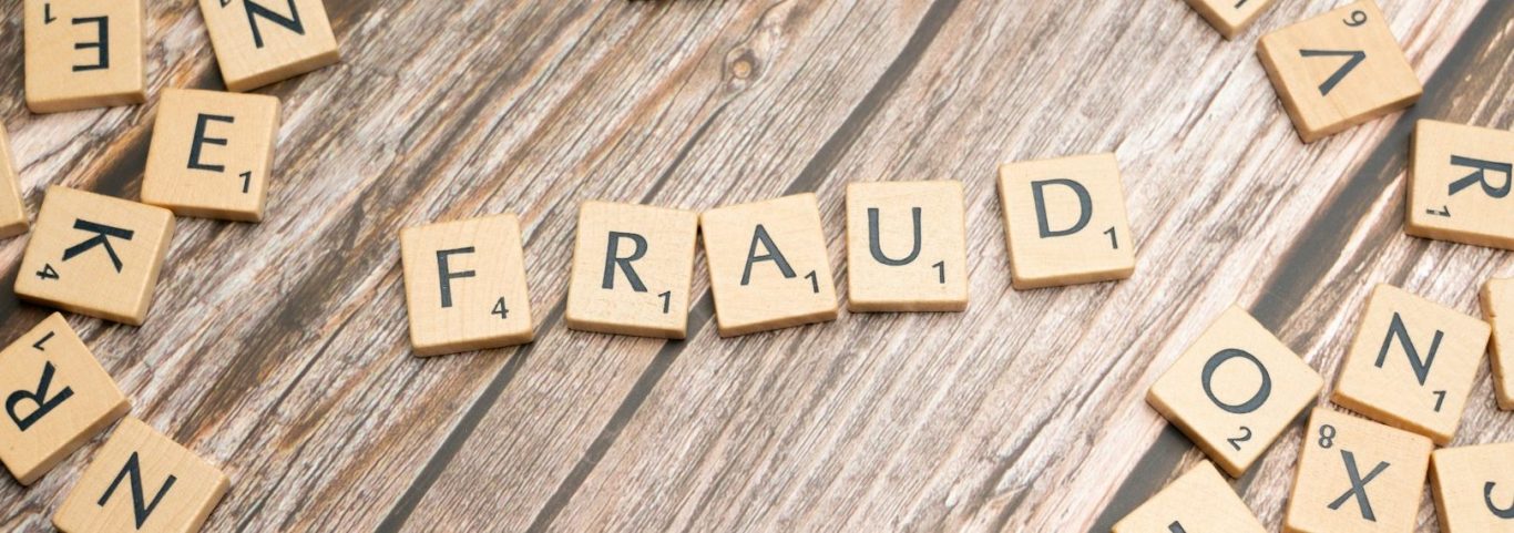 Buchstabenwürfel mit dem Wort "FRAUD" und verstreuten Buchstaben auf einem Holztisch.