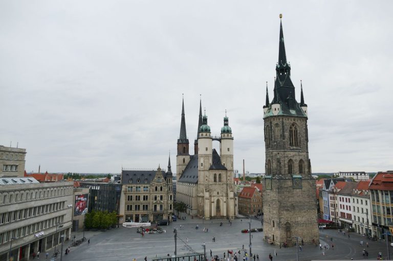 Stadtansicht von Halle mit historischen Gebäuden und Türmen unter einem bewölkten Himmel.