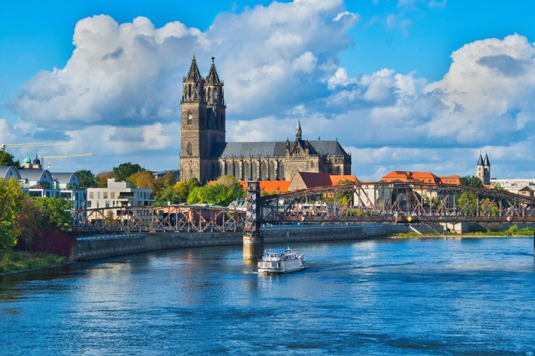Blick auf Magdeburg mit Fluss, Häusern und einer Kirche unter bewölktem Himmel.