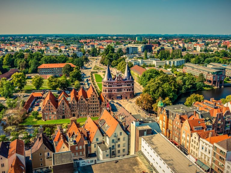 Luftaufnahme der Stadt Lübeck mit roten Dächern und historischen Gebäuden umgeben von Grün.