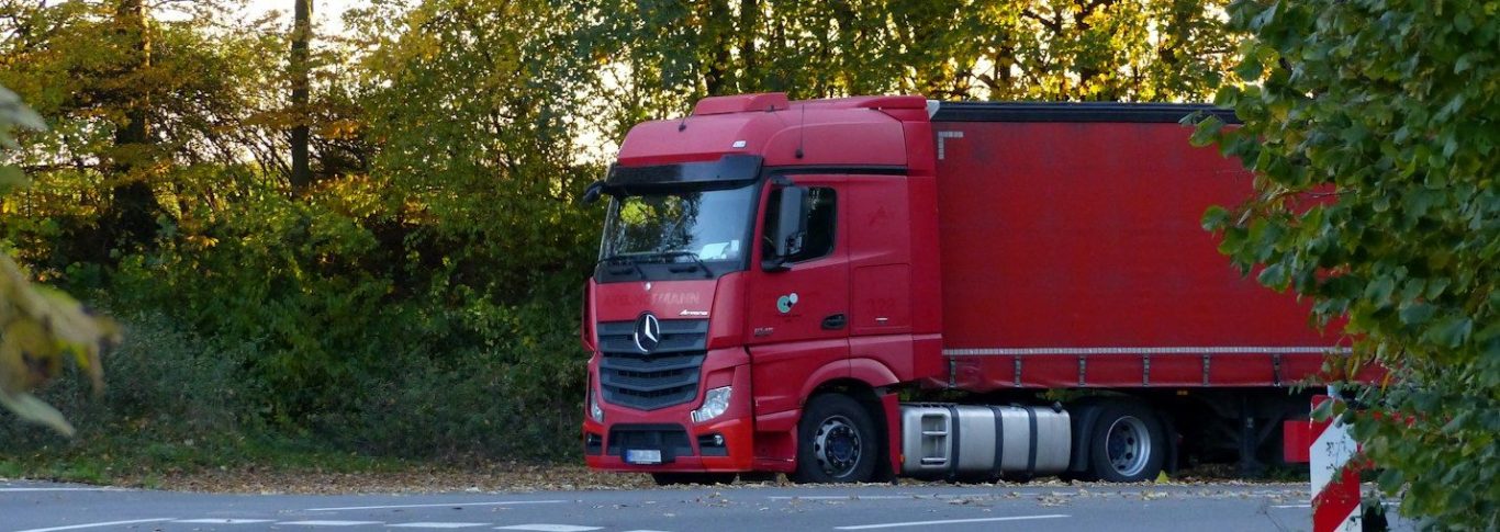 Ein roter Lastwagen steht an einer Straßenbiegung, umgeben von Bäumen.