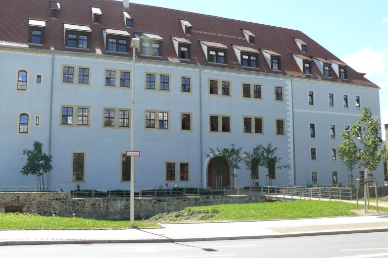 Schloß Osterstein mit roten Dachziegeln, grüner Umgebung und mehreren Fenstern.