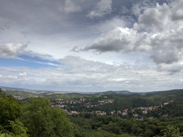 Blick auf eine bewaldete Landschaft in Thüringen mit Wolken und einem kleinen Dorf im Tal.