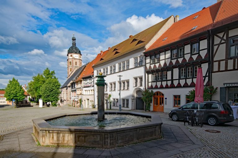Marktplatz mit Brunnen, historischen Gebäuden und Kirche im Hintergrund.