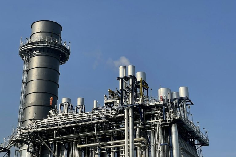 Industrieanlage in Schwedt mit hohen Schornsteinen und Rohren gegen blauen Himmel.