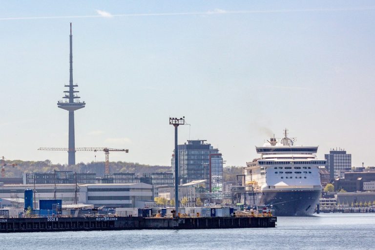 Hafenansicht von Kiel mit einem Kreuzfahrtschiff und dem Fernsehturm im Hintergrund.