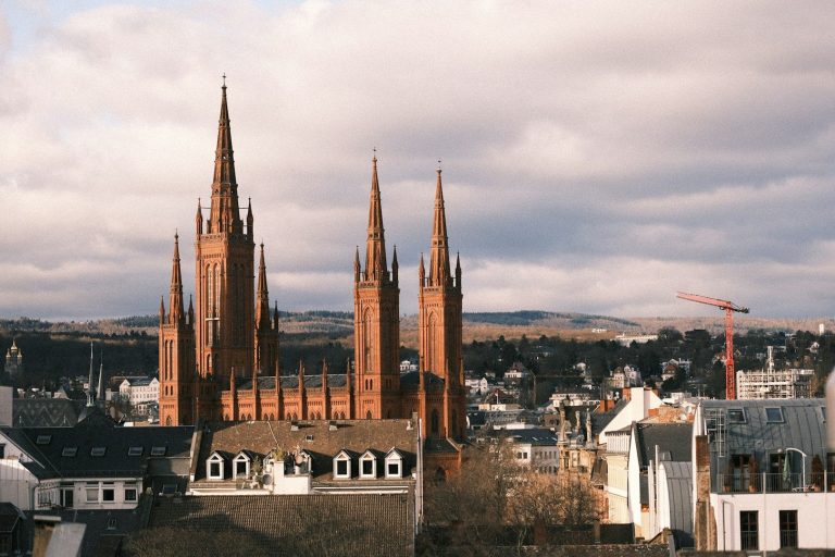 Blick auf eine historische Kirche in Wiesbaden mit hohen Türmen und modernem Stadtbild im Vordergrund.