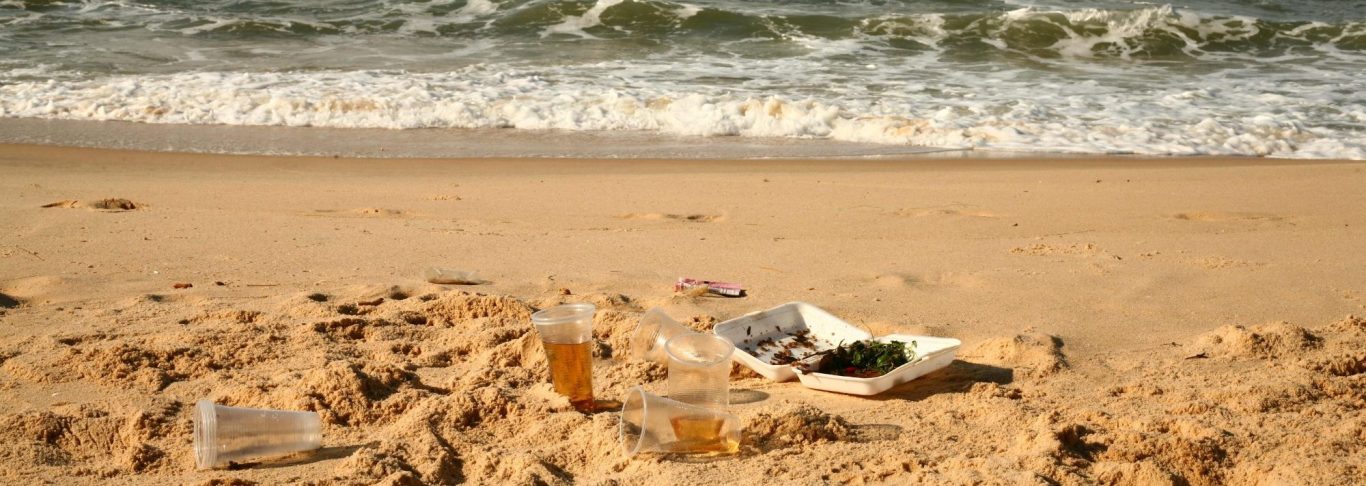 Aufklärungen und Ermittlungen in Mecklenburg-Vorpommern | Wirtschaftsdetektei Abgelegte Getränke und Müll liegen im Sand am Strand, mit Wellen im Hintergrund.