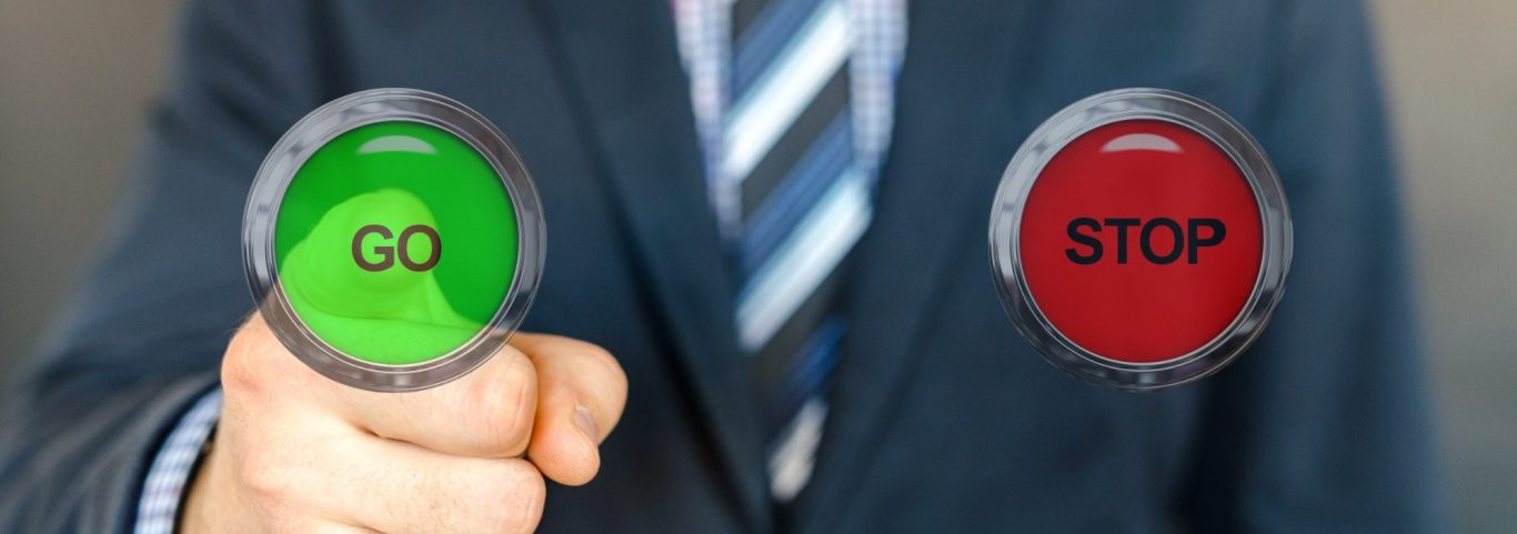 Mann hält eine grüne "GO"- und eine rote "STOP"-Taste in den Händen.