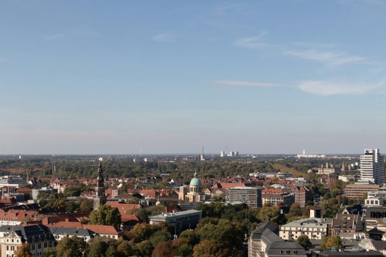 Blick auf die Stadt Hannover mit grünen Flächen und modernen Gebäuden unter klarem Himmel.
