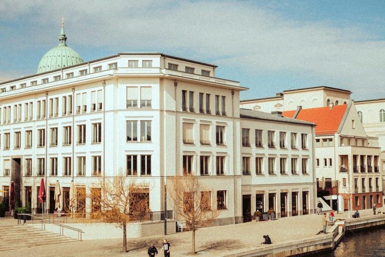 Moderne Gebäudefassade in Potsdam in hellen Farben mit einem grünen Kuppeldach und umgebenden Bäumen.