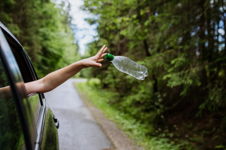 Hand wirft eine leere Plastikwasserflasche aus dem Fenster eines Fahrzeugs.