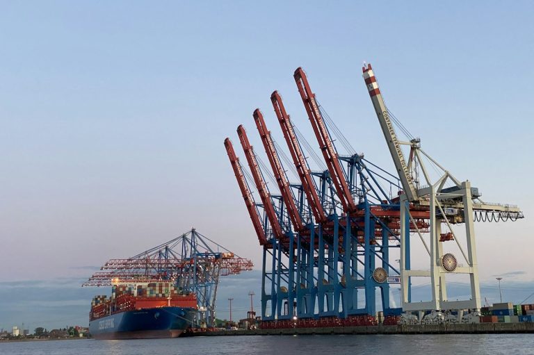 Hamburg Hafen mit großen Kränen und einem Containerschiff im Hintergrund bei Sonnenuntergang.