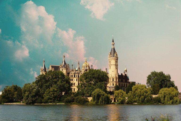 Schloss im Wasser, umgeben von Bäumen und einem blauen Himmel mit Wolken. Schwerin