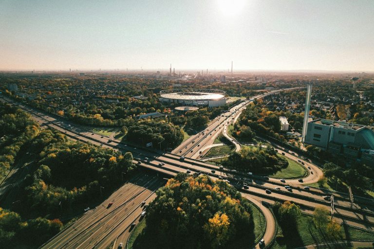 Überblick auf eine Stadtlandschaft mit Autobahnen und grünen Parks im Vordergrund.
