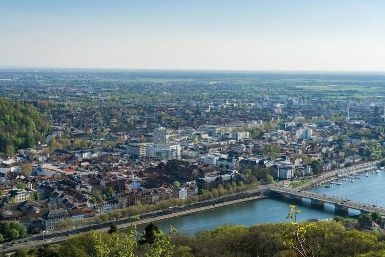 Panoramablick auf die Stadt Heidelberg mit Fluss und sanften Hügeln im Hintergrund.