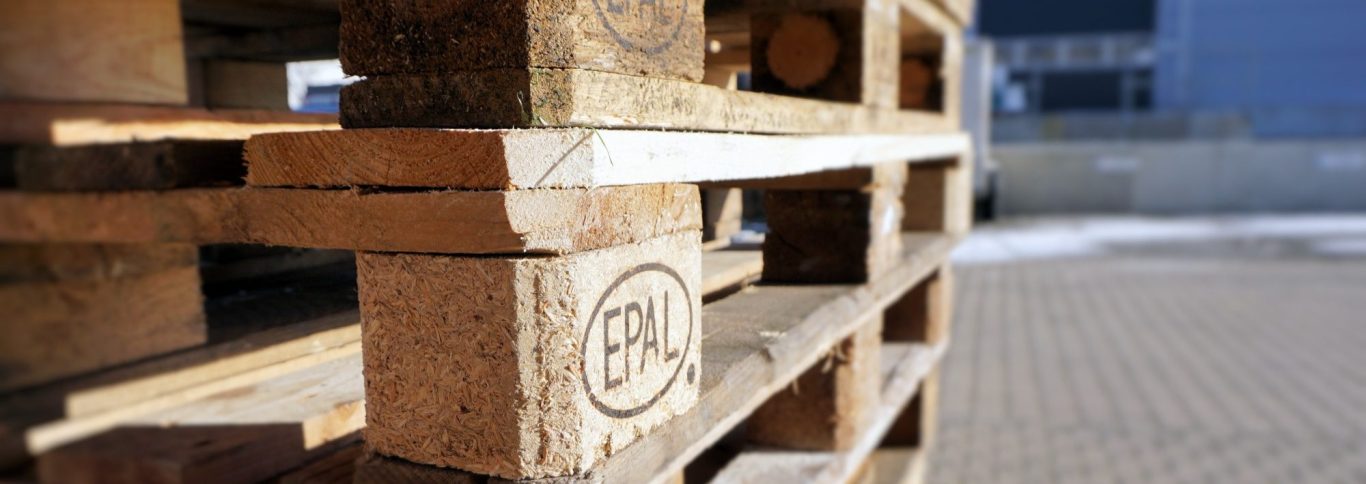Holzpalette mit gestapelten Brettern, leicht unscharf im Vordergrund.