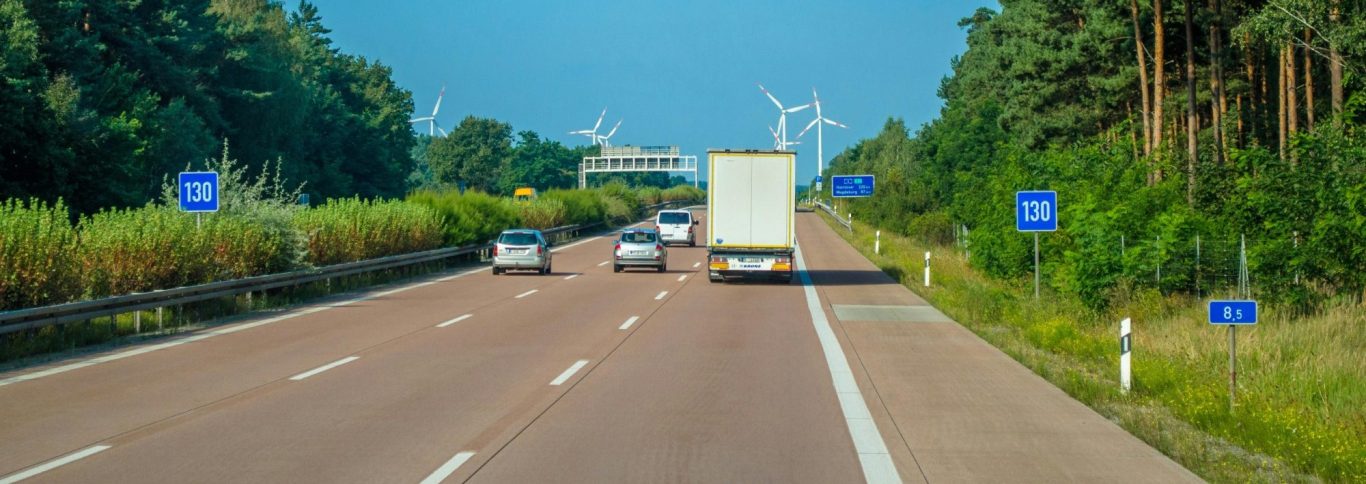 Autobahn mit Lkw und anderen Fahrzeugen, umgeben von Bäumen und Schildern.