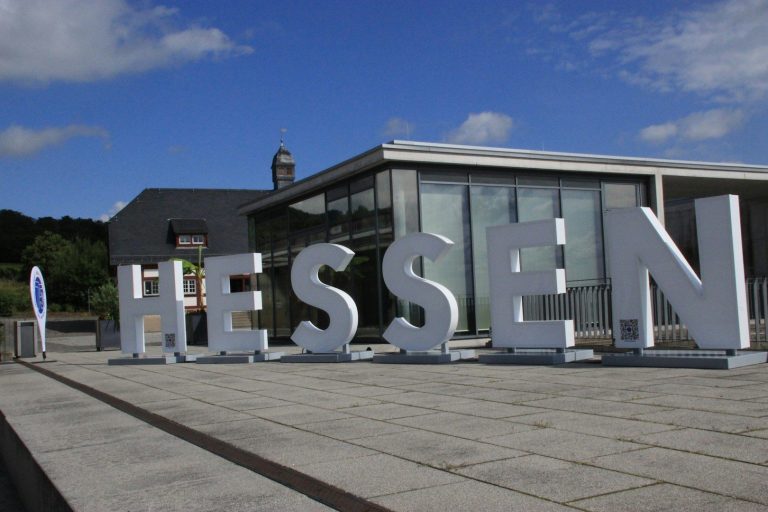 Große, weiße Buchstaben bilden das Wort "HESSEN" vor einem modernen Gebäude.