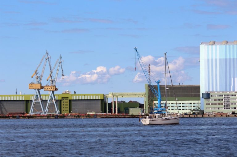 Hafenansicht von Stralsund mit Kränen, einem Segelboot und moderne Gebäude im Hintergrund.