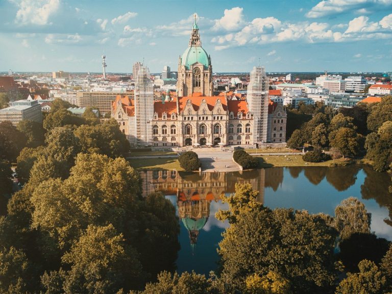 Das Neue Rathaus in Hannover, umgeben von Bäumen und einem reflektierenden Teich.