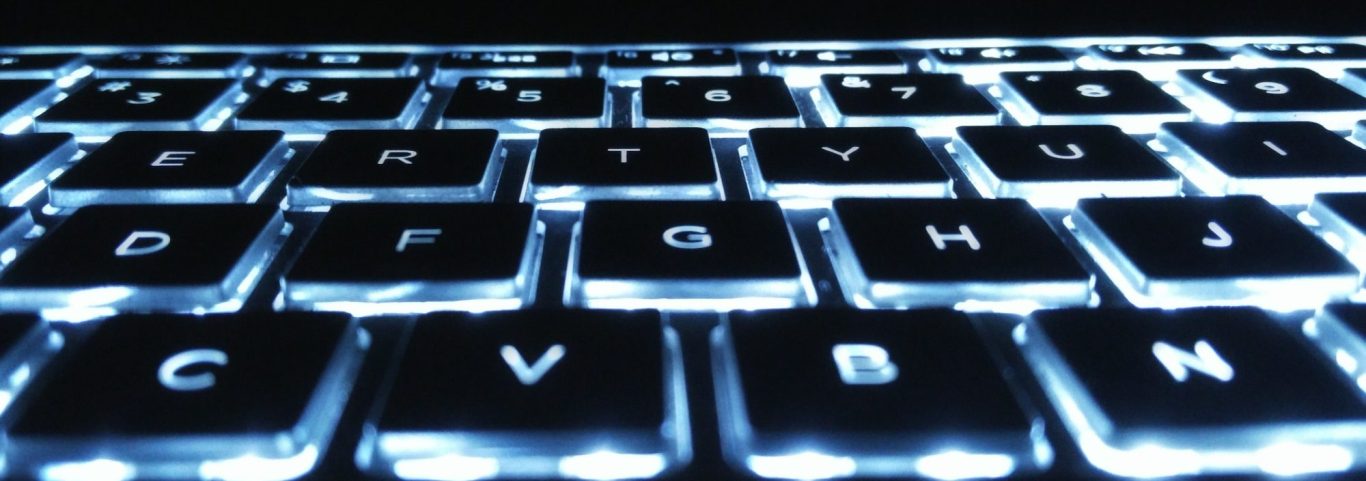 Nahaufnahme einer beleuchteten Tastatur mit dunklen Tasten und leuchtenden Buchstaben.